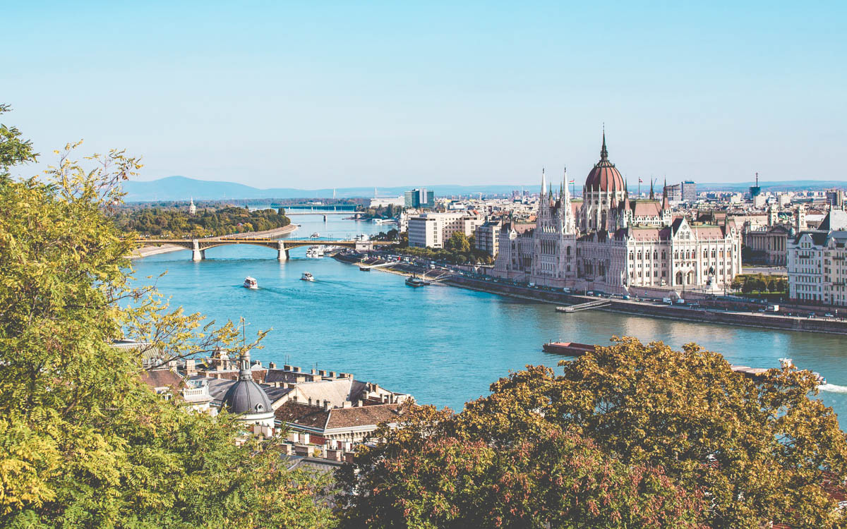 Utsikt över floden Donau i Budapest Ungern. Solen lyser på husen längs floden. Broar länkar samman de två stadssidorna.