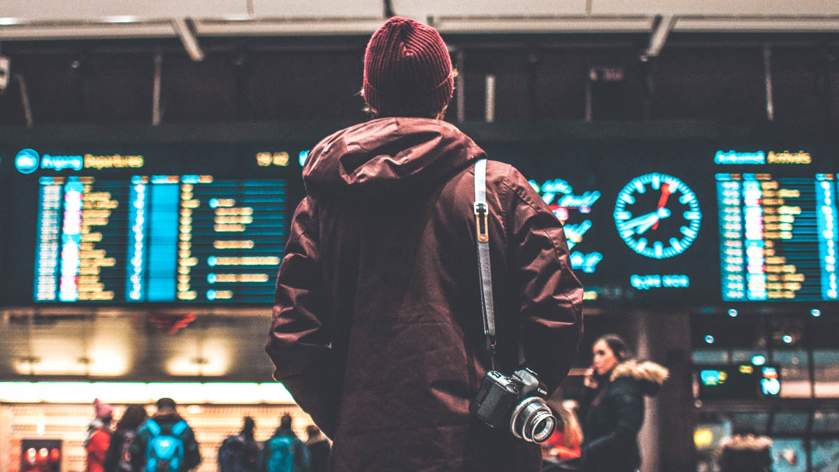 Man står med ytterkläder på sig på en flygplats och letar efter sin flygavgång