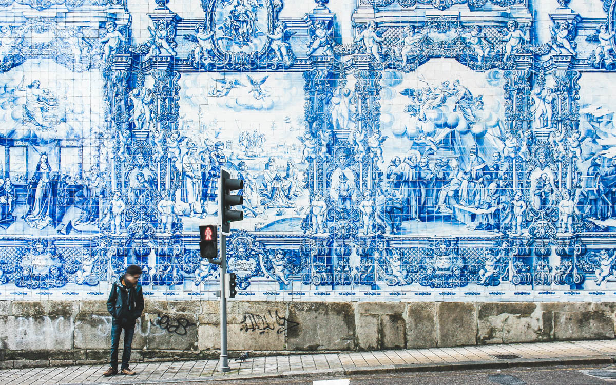 Man som står vid en vägg fylld med vacker blå portugisisk mosaik, Azulejos som illustrerar Portos historia. Porto, Portugal.