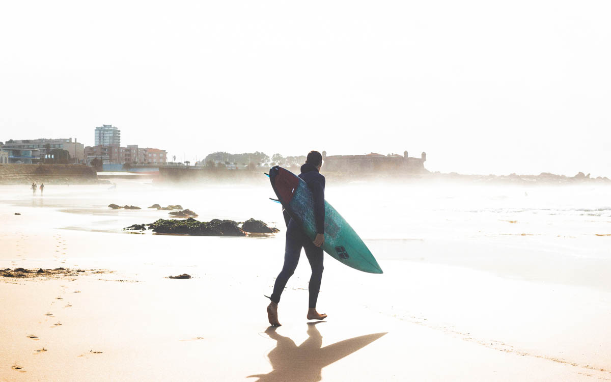 Man som går på stranden i Matosinhos, Porto, Portugal, med surfbräda under armen på väg ut i vattnet för att surfa.