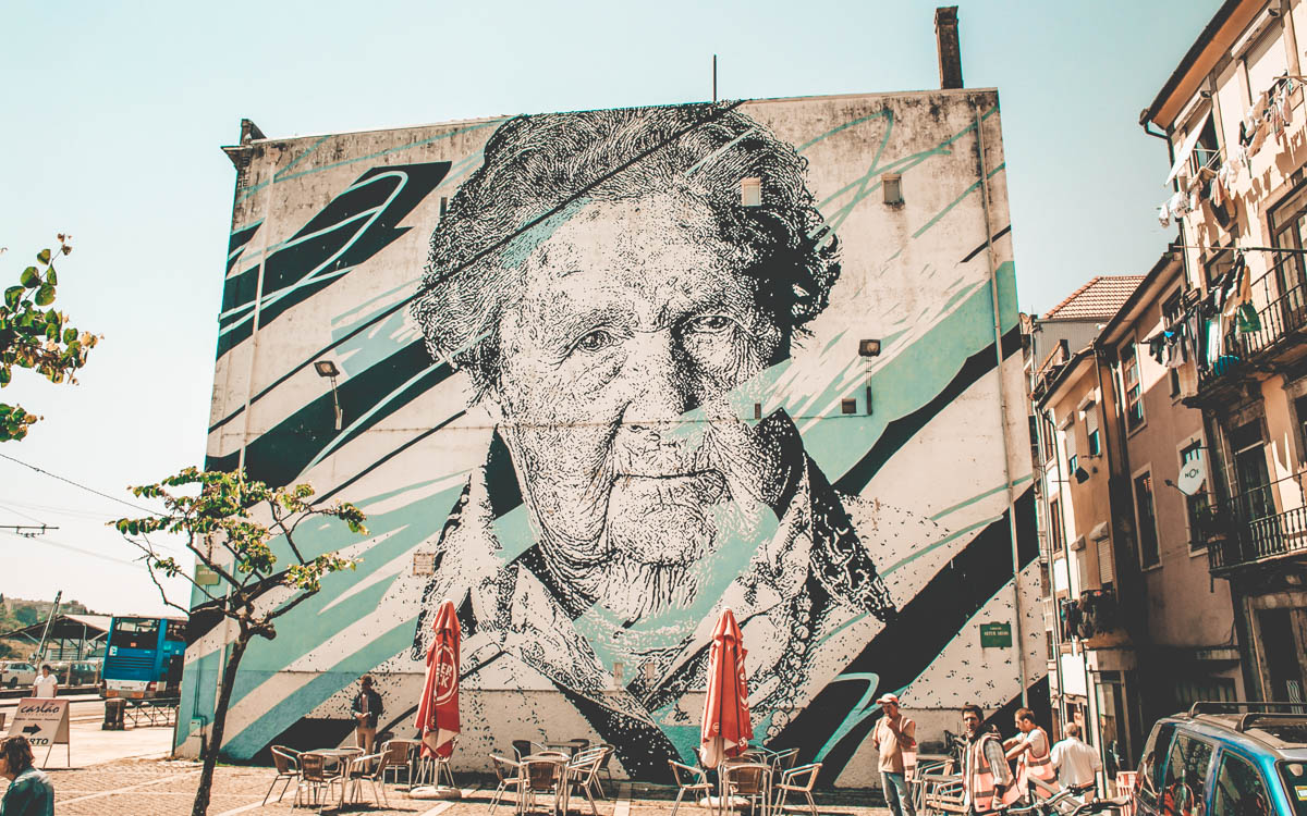 stor graffitimålning av en gammal dam på vägg vid ett kafé i porto portugal